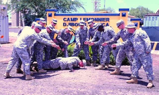 12 Officers with Task Force Longrifles team up to 'order' their former OCS instructor do pushups, here at Camp Lemonnier, Djibouti in Africa.  Photo by Sgt. Alexa Becerra, 2-138th PAO